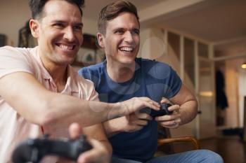 Loving Same Sex Male Couple Sitting On Sofa At Home Gaming Together