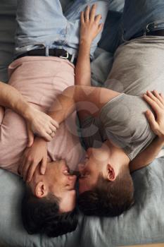 Overhead Shot Of Loving Same Sex Male Couple Lying On Bed At Home Hugging Together