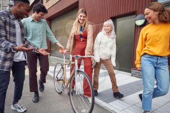 Group Of Multi-Cultural Friends Walking On City Street With Sustainable Bamboo Bicycle