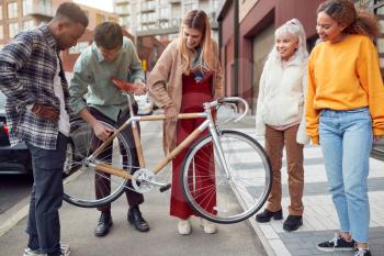 Group Of Multi-Cultural Friends On City Street Lifting Sustainable Bamboo Bicycle
