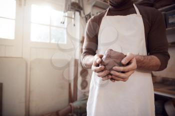 Close Up Of Male Potter Wearing Apron Holding Lump Of Clay In Ceramics Studio