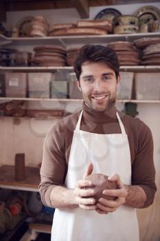 Portrait Of Male Potter Wearing Apron Holding Lump Of Clay In Ceramics Studio