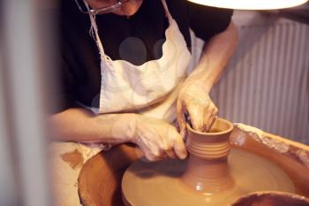 Close Up Of Female Potter Shaping Clay For Pot On Pottery Wheel In Ceramics Studio