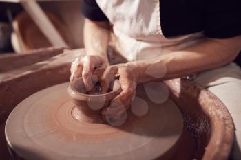 Close Up Of Female Potter Shaping Clay For Pot On Pottery Wheel In Ceramics Studio