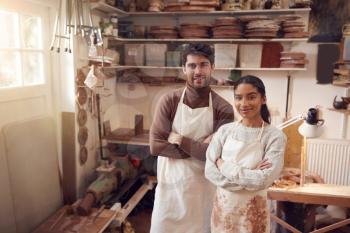 Portrait Of Couple Running Bespoke Pottery Business Working In Ceramics Studio Together