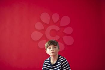 Portrait Of Thoughtful Young Boy Against Red Studio Background