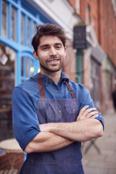 Portrait Of Male Small Business Owner Wearing Apron Standing Outside Shop On Local High Street