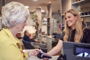 Senior Woman Making Contactless Payment To Stylist In Salon With Credit Card