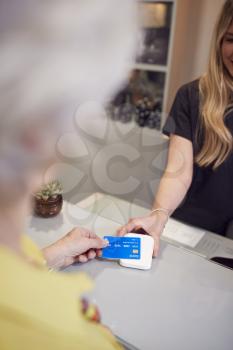 Close Up Of Senior Woman Making Contactless Payment To Stylist In Salon With Credit Card