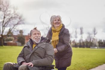 Senior Woman Pushing Senior Man In Wheelchair Outdoors In Fall Or Winter Park