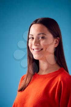 Studio Portrait Of Confident Young Woman Looking Into Camera Against Blue Background