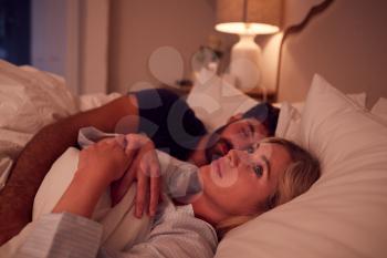 Couple With Woman Lying In Bed Awake At Night Suffering With Insomnia