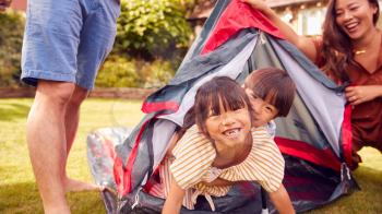 Asian Family In Garden At Home Putting Up Tent For Camping Trip Together