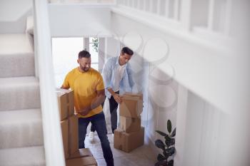 Excited Male Couple Carrying Boxes Through Front Door Of New Home On Moving Day