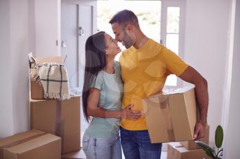 Loving Couple Carrying Boxes Through Front Door Of New Home On Moving Day