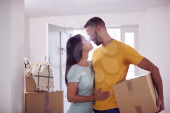 Loving Couple Carrying Boxes Through Front Door Of New Home On Moving Day
