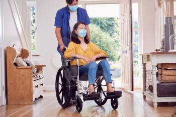 Mature Asian Man Wearing Face Mask Pushing Wife In Wheelchair At Home During Health Pandemic