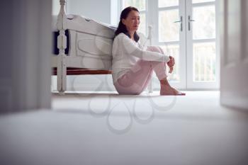 Unhappy And Depressed Mature Asian Woman In Pyjamas Sitting On Bedroom Floor