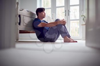 Unhappy And Depressed Mature Asian Man In Pyjamas Sitting On Bedroom Floor