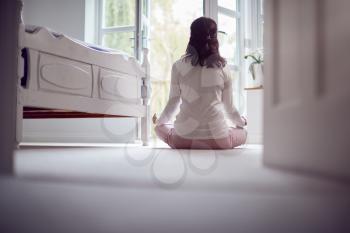 Rear View Of Mature Asian Woman In Pyjamas Sitting On Bedroom Floor Meditating In Yoga Pose