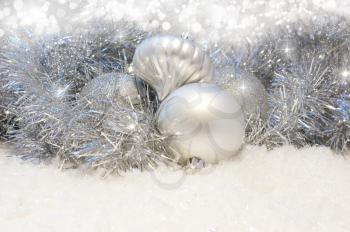 Silver Christmas baubles nestled in tinsel and snow