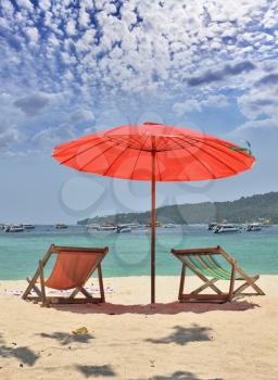 Tropical paradise on the shores of the azure sea. Red beach umbrella and deck chairs on the white sand