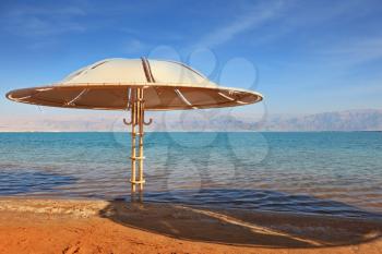 A magnificent beach with clean yellow sand on the shore of the Dead Sea. Guests of the hotel - beach umbrellas 