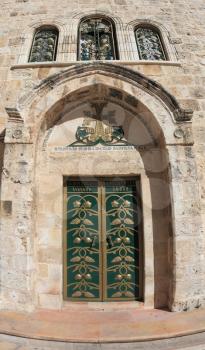 The side entrance to the Temple of the Holy Sepulcher lit bright sun. Picturesque green door decorated with gold ornaments. Above the door of the golden cross and three semicircular windows