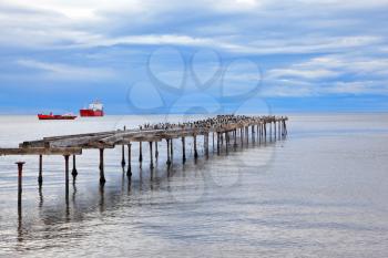 Abandoned pier. Old dilapidated pier in the Strait of Magellan. In the distance the two cargo ships