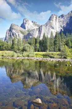 Phenomenally scenic Yosemite Valley. The mirror surface of the Merced river reflects the picturesque cliff tops and blue sky