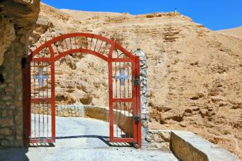 Decorative red gate with a cross on a mountain road going to the temple. Wadi Kelt near Jerusalem