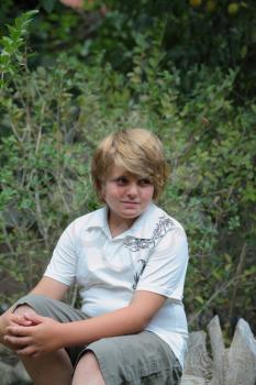A beautiful blond boy poses for the photographer, sitting in the garden