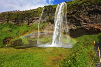 Seljalandsfoss waterfall in Iceland. Sunny day in July. Large rainbow decorates  drop of water