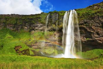  Sunny day in July. Seljalandsfoss waterfall in Iceland. Large rainbow decorates a drop of water