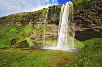 Large rainbow decorates a drop of water. Seljalandsfoss waterfall in Iceland. Summer sunny day 
