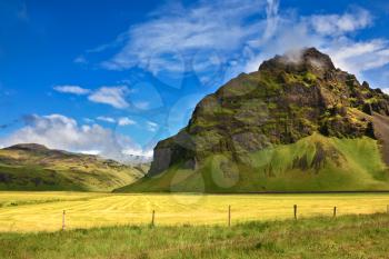 Typical landscape for the summer in Iceland. Bright green and yellow farm fields at the foot of steep mountains. 