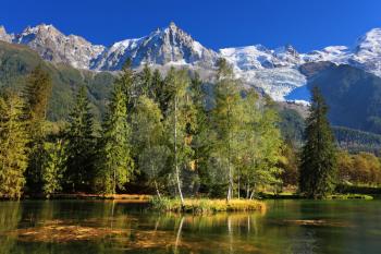 Cozy urban park in Chamonix, Provence. Snowy Alps picturesquely surrounded by evergreen trees and lake