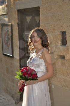 The beautiful bride with a wedding bouquet has thoughtfully leant against a wall of old city.