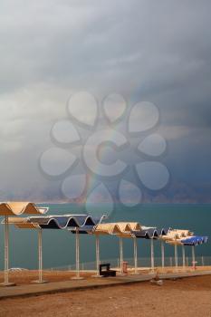 Winter on the Dead Sea. Empty beach umbrellas, green water and magnificent rainbow