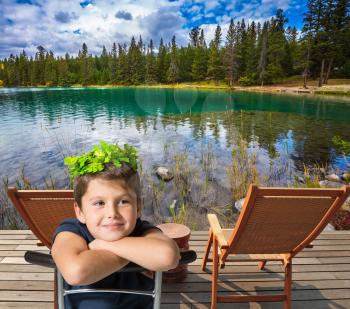 The Rocky Mountains of Canada. Two convenient chaise lounges on the bank of round lake. The beautiful boy in a carnival wreath