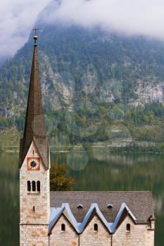 Slender belfry and Lutheran church on the shore of Lake Hallstatt. On the opposite shore of the lake - the beautiful mountains overgrown with forests. The most picturesque small town in Austria - Hall