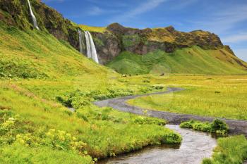 Iceland in July. Warm summer day. Selyalandfoss waterfall and picturesque flowering fields and streams
