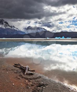 After the storm. Gray lake in the national park Torres del Paine in Chilean Patagonia. Clouds are reflected in ice water of the lake. The blue iceberg is in the distance visible