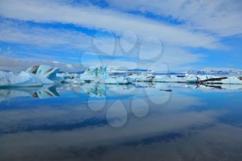 Blue and turquoise icebergs and cirrus clouds are reflected in the Bay Jökulsárlón in Iceland. Sunrise. Reflection