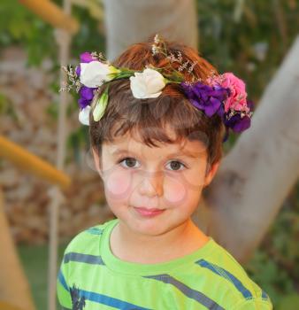 Very beautiful little boy posing in the garden. This holiday - his birthday. He is crowned with a wreath of flowers