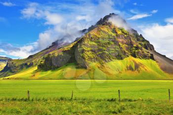 Typical landscape for the summer in Iceland. Bright green floral and farmland at the foot of steep mountains. 