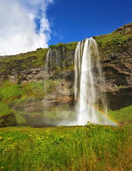 Seljalandsfoss waterfall in Iceland. Summer sunny day. Large rainbow decorates a drop of water