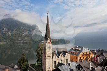  The most picturesque small town in Austria - Hallstatt. Slender belfry and Lutheran church on the shore of Lake Hallstatt. On the opposite shore of the lake - the beautiful mountains overgrown with f