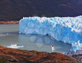 Giant lake glacier of Perito Moreno. The woman ashore in a white suit for yoga carries out a pose Tree