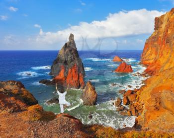 The woman ashore in a white suit for yoga carries out a pose Tree. Atlantic storms. Colorful pinnacles lit sunset. Arid eastern tip of the island of Madeira